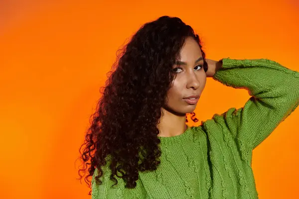 Une femme frappante dans un pull vert et boucles captive avec sa pose confiante. — Photo de stock