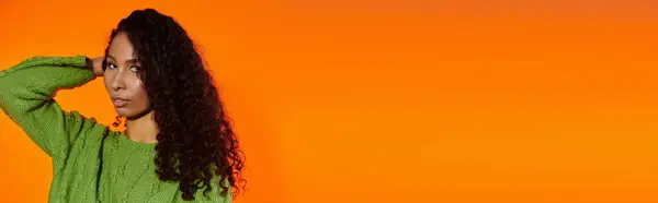 Woman with long curly hair captures attention with her confident pose in front of orange backdrop. — Stock Photo