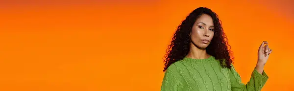 In a striking green sweater, a beautiful woman poses confidently against a warm orange background. — Stock Photo