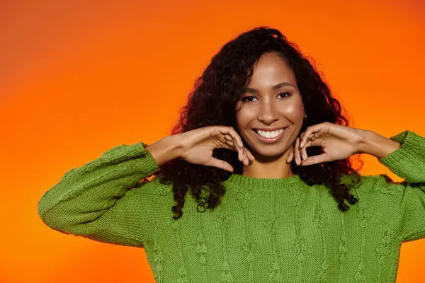 A cheerful woman with curly hair smiles brightly while posing in a cozy green sweater. — Stock Photo