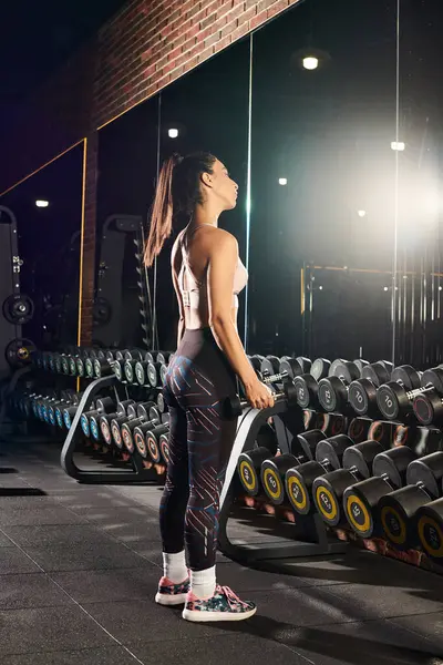 Focused woman performs strength training with weights in a vibrant gym setting. — Stock Photo