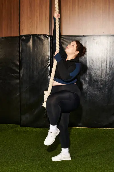 Woman engages in a focused rope climbing exercise within a well equipped gym — Stock Photo