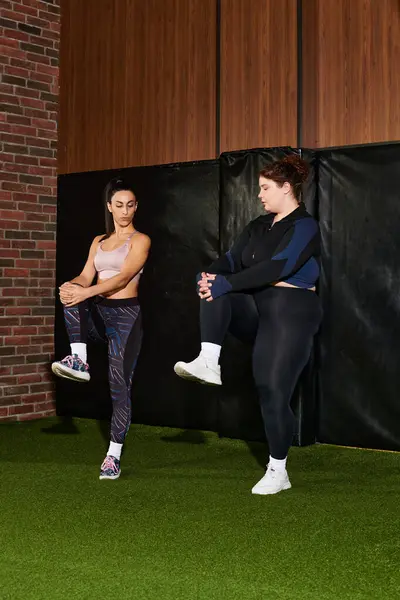 Two women engage in a dynamic stretching routine in a modern gym setting. — Stock Photo