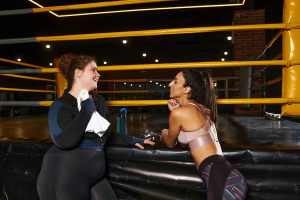 Two women share a lighthearted conversation post workout in a modern gym environment. — Stock Photo