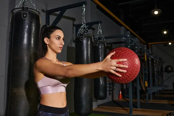 Una mujer dedicada se involucra en una poderosa rutina de pelota de medicina en un vibrante gimnasio. — Stock Photo