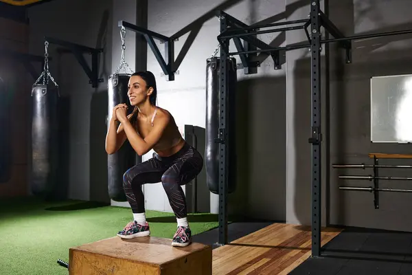 Mujer dedicada realiza sentadillas cuadro, mostrando fuerza y determinación en un gimnasio animado. - foto de stock