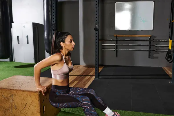 Femme dédiée effectue des trempettes triceps sur une boîte en bois dans un cadre de gymnase dynamique. — Photo de stock