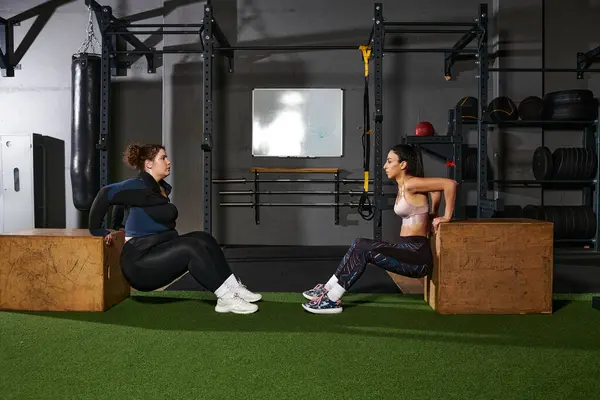 Friends perform tricep dips together at a modern gym while encouraging each other. — Stock Photo