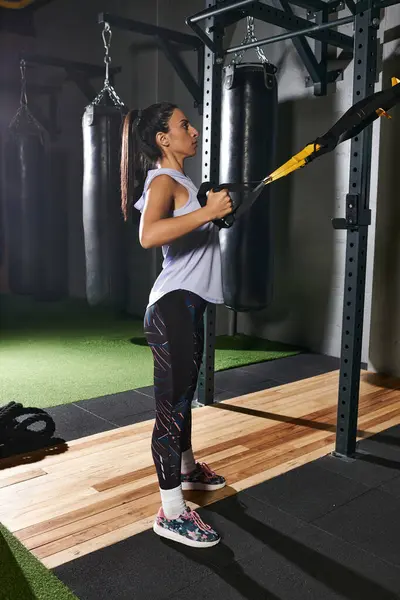 Mujer dedicada se centra en mejorar la fuerza con el entrenamiento TRX en un entorno de gimnasio vibrante. - foto de stock