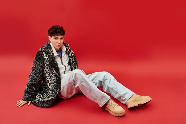 Handsome man seated against a bold red background, displaying unique fashion choices and flair. — Stock Photo