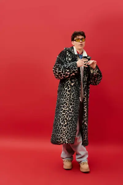A charming man stands against a vibrant red background in a leopard print coat and trendy glasses. — Stock Photo
