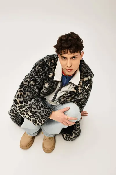 Handsome man in trendy outfit poses thoughtfully while crouching on a clean backdrop. — Stock Photo