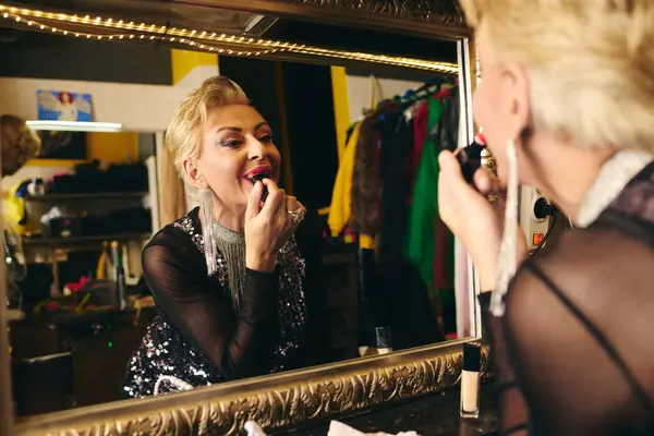 Une drag queen vibrante applique un rouge à lèvres audacieux devant un miroir, se préparant pour un spectacle festif. — Photo de stock