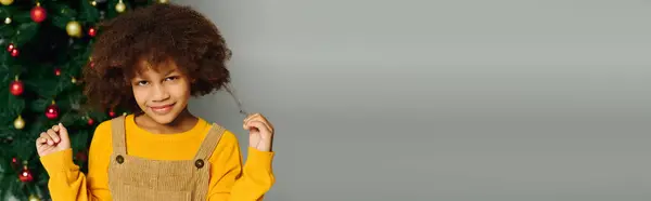 Una ragazza sorride felice, gioca con i capelli, circondata da decorazioni natalizie e un albero. — Foto stock