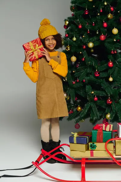 A cheerful young girl stands smiling with a present, surrounded by Christmas decorations. — Stock Photo