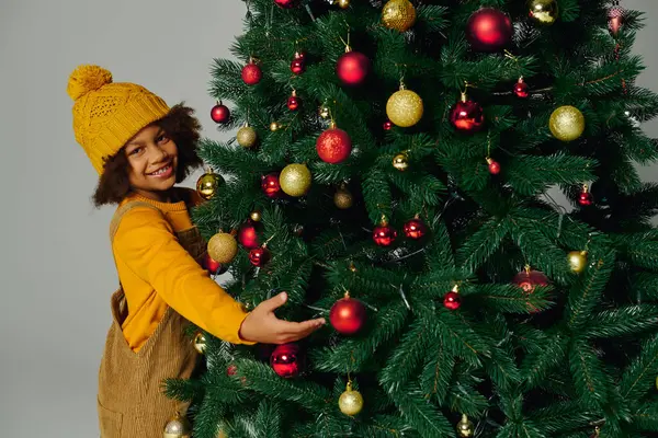 Girl smiles while placing colorful ornaments on a Christmas tree for the holiday. — Stock Photo