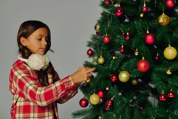 Joyful girl adds colorful decorations to a Christmas tree celebrating the holiday spirit. — Stock Photo