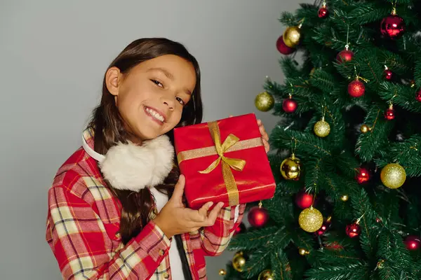 Delighted girl shows off her gift while celebrating Christmas 2025 by a festive tree. — Stock Photo