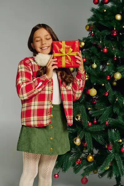 Girl delights in a beautifully wrapped present near a decorated Christmas tree filled with joy. — Stock Photo