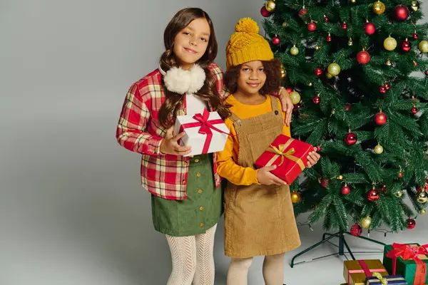 Two happy girls hold gifts by a beautifully decorated Christmas tree. — Stock Photo