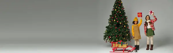 Two excited kids enjoy Christmas by a beautifully decorated tree and presents. — Stock Photo