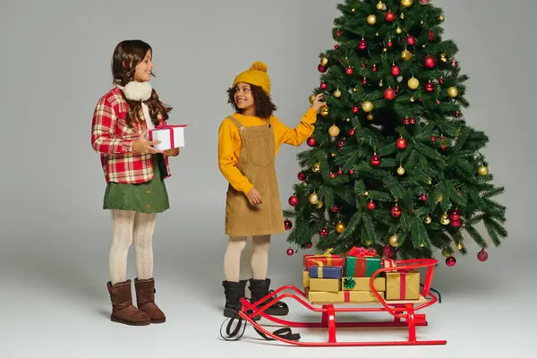 Girls excitedly decorate a Christmas tree with ornaments and gifts around them for 2025. — Stock Photo