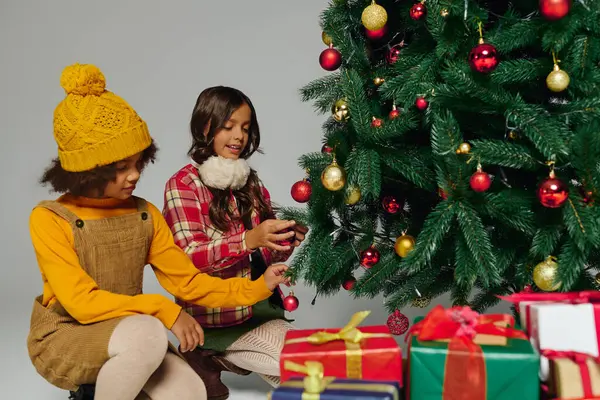 Dos niños colocan felizmente adornos en un árbol de Navidad festivo, rodeado de regalos envueltos. — Stock Photo