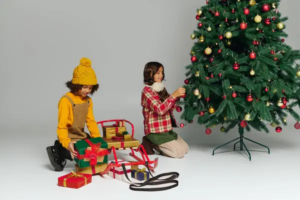 Due ragazze gioiose stanno decorando un vibrante albero di Natale pieno di ornamenti e regali. — Foto stock
