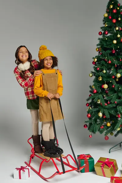 Dos chicas alegres disfrutan de un momento lúdico en un trineo rodeado de regalos navideños. — Stock Photo