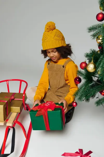 A little one in a bright yellow outfit eagerly unwraps presents near the Christmas tree. — Stock Photo