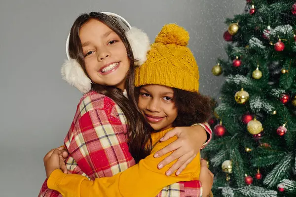 Two joyful girls embrace warmly, wearing winter attire amid a festive holiday atmosphere. — Stock Photo