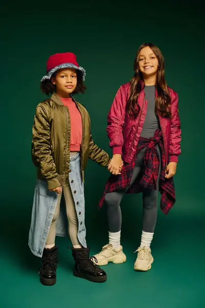 Two joyful girls in stylish Christmas outfits hold hands against a colorful backdrop. — Stock Photo