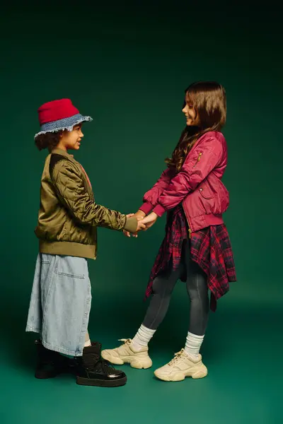 Two girls hold hands, sharing laughter and dresses in vibrant attire for Christmas 2025. — Stock Photo