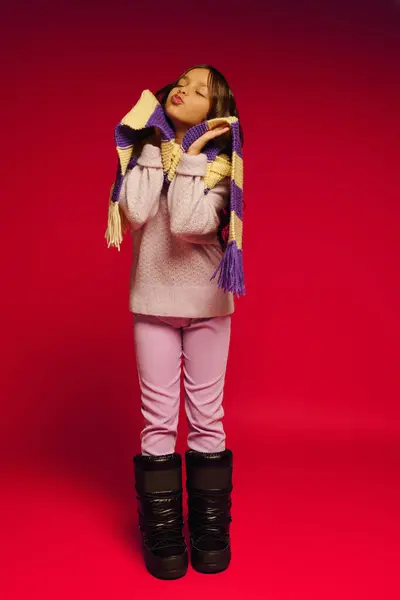 A joyful girl poses with a playful expression, featuring a colorful scarf and winter boots. — Stock Photo