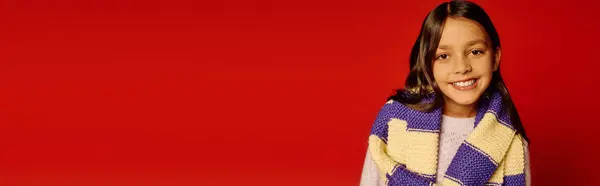 Young girl showcases a colorful knitted scarf while radiating joy in a holiday setting. — Stock Photo