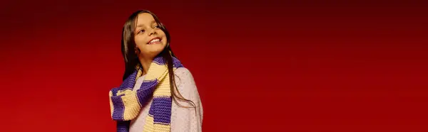 A cheerful girl wearing a colorful scarf smiles warmly, embracing the joy of Christmas 2025. — Stock Photo