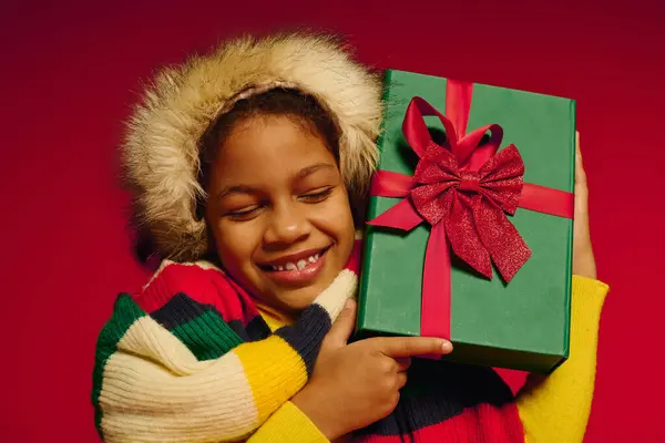 A smiling girl embraces a green gift, radiating excitement and holiday cheer during Christmas. — Stock Photo