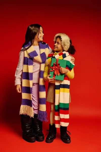 Two energetic girls dressed warmly share smiles while holding gifts during Christmas festivities. — Stock Photo