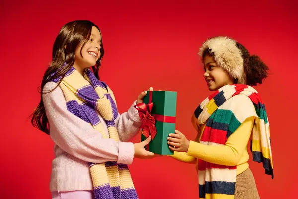 Two girls share a delightful moment exchanging a wrapped Christmas gift in 2025. — Stock Photo