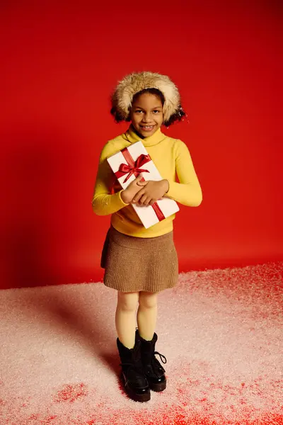 Delighted girl dressed in festive attire stands excitedly with a present for Christmas 2025. — Stock Photo