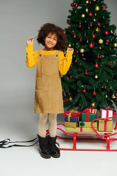Girl wearing a stylish outfit stands beside a decorated tree, beaming with holiday spirit. — Stock Photo