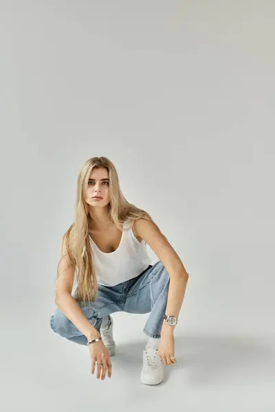 A beautiful young woman with long blonde hair poses gracefully in casual attire in a studio. — Stock Photo