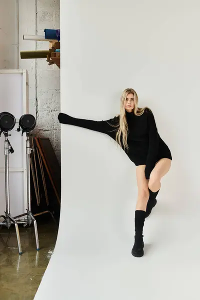 A beautiful woman with long blonde hair poses in a sleek black outfit in the studio. — Stock Photo