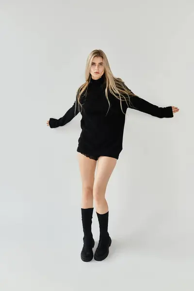 A beautiful young woman with long blonde hair showcases trendy black fashion in a minimalist studio. — Stock Photo