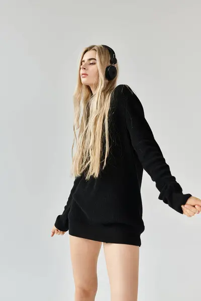 A beautiful young woman poses confidently in a stylish black outfit while listening to music. — Stock Photo