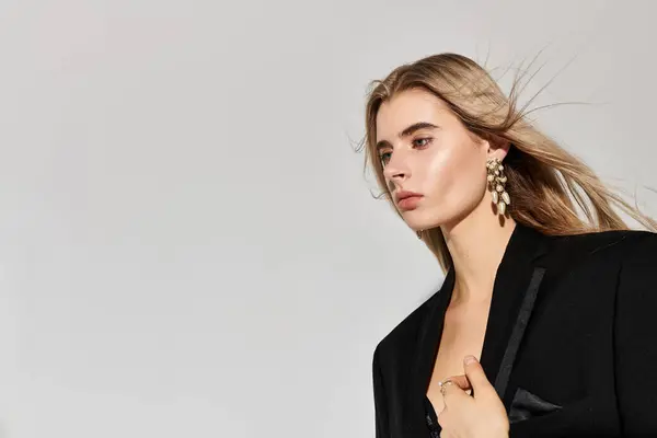 A confident young woman with long blonde hair poses elegantly in a chic black outfit. — Stock Photo