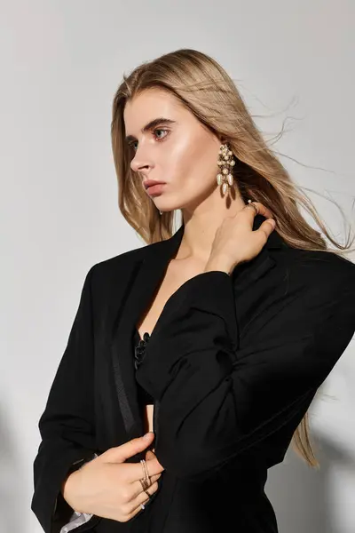 Jeune femme aux longs cheveux blonds pose gracieusement dans une tenue noire, respirant la confiance et le style. — Photo de stock