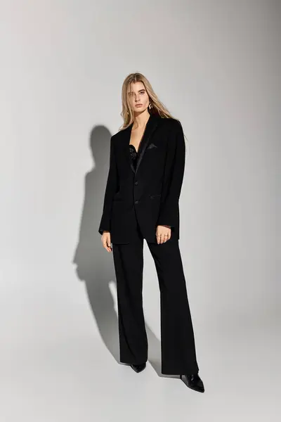 A stunning model with long blonde hair poses confidently in stylish black attire in a studio. — Stock Photo