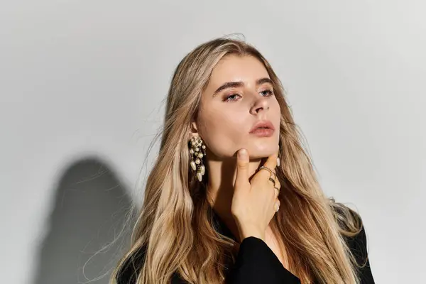 In a stylish studio, a beautiful young woman with long blonde hair poses elegantly in black attire. — Stock Photo