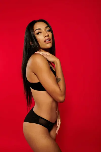 Una joven afroamericana posa con confianza en ropa interior con estilo sobre un audaz telón de fondo rojo. - foto de stock